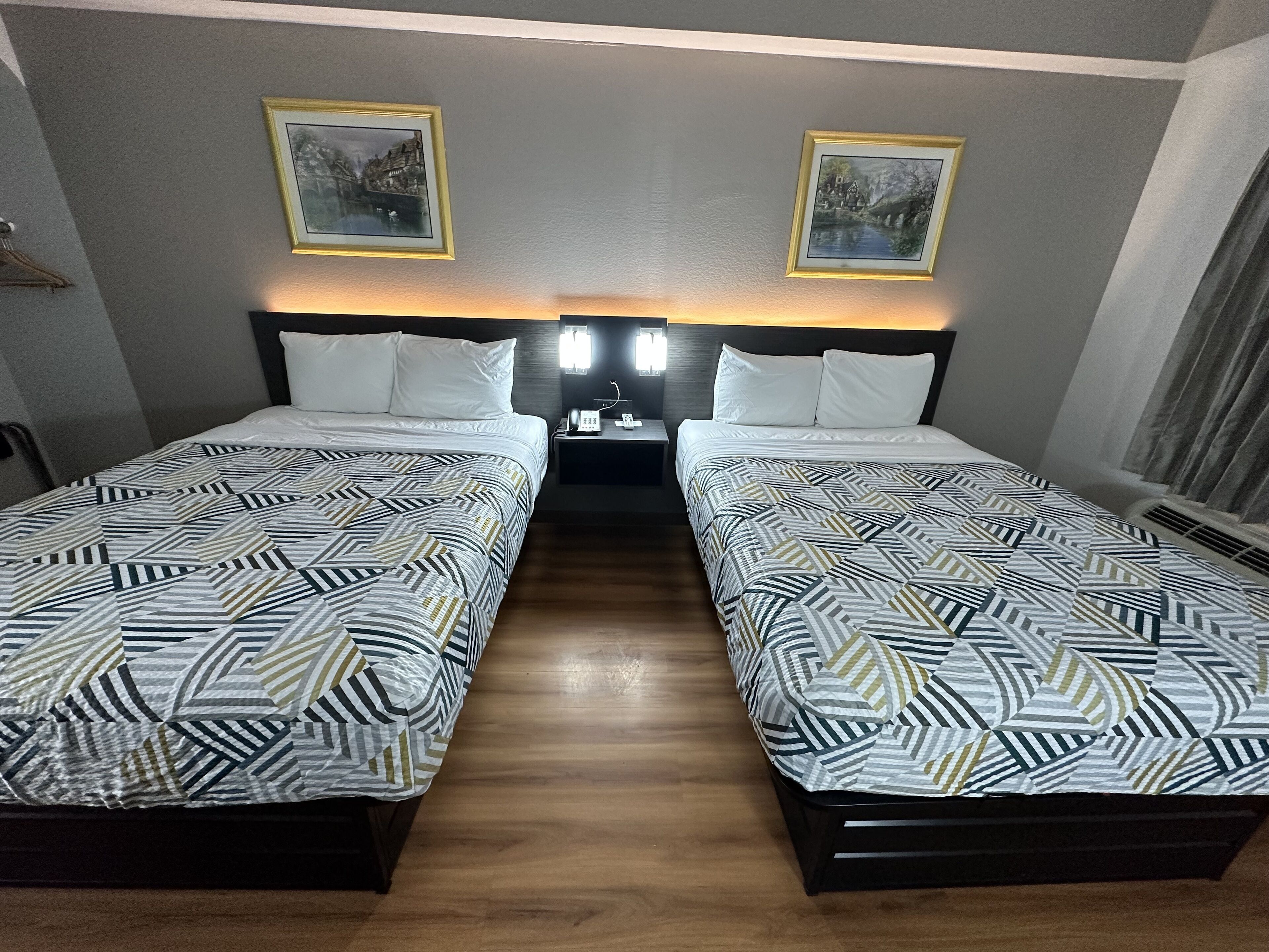 Une chambre d’hôtel avec deux lits, chacun recouvert d’une couvre-lit à motifs, une table de chevet avec un téléphone et deux tableaux encadrés accrochés au mur.