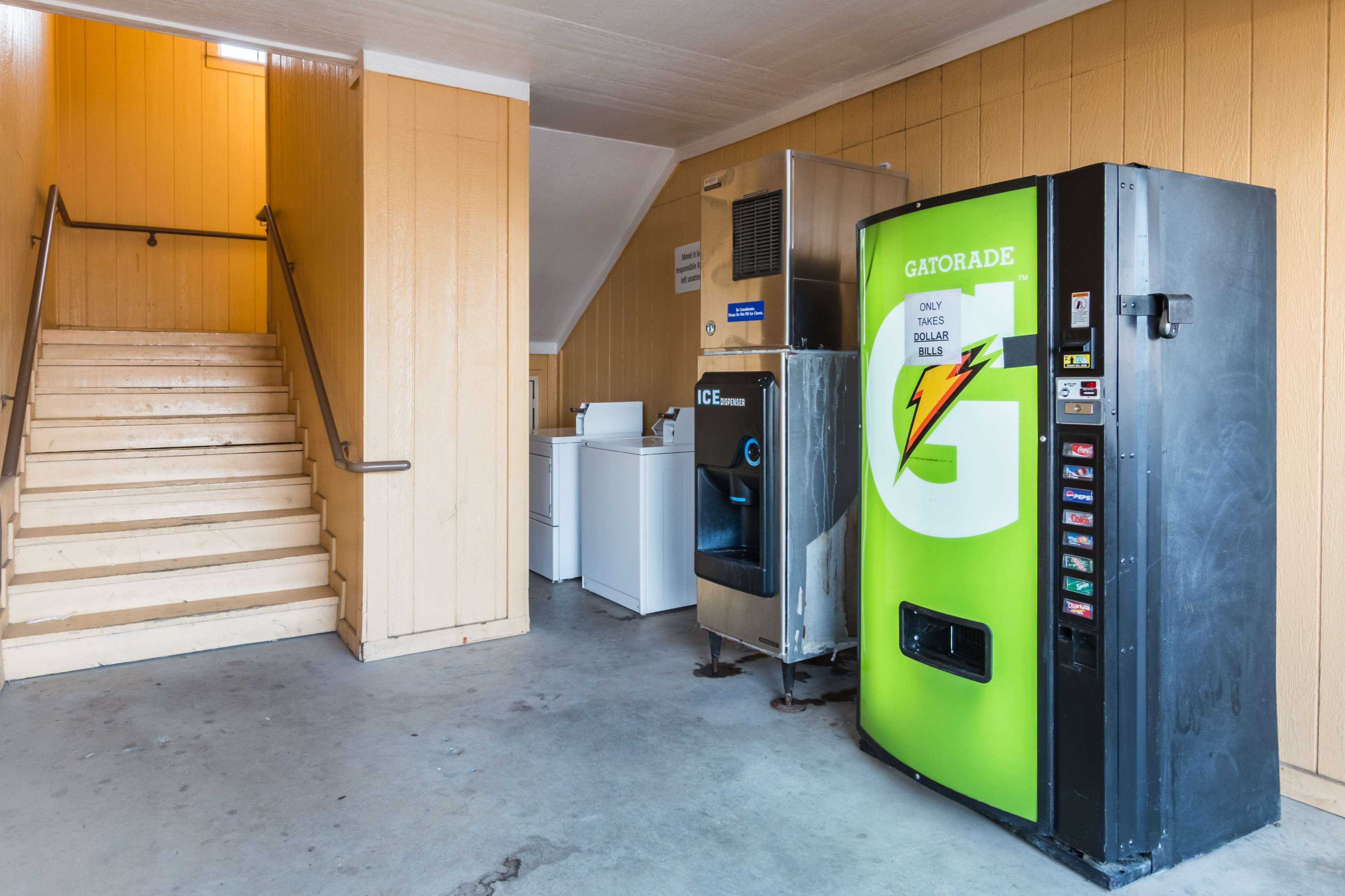 A Gatorade vending machine, a refrigerator, and a staircase in a room with wooden walls.