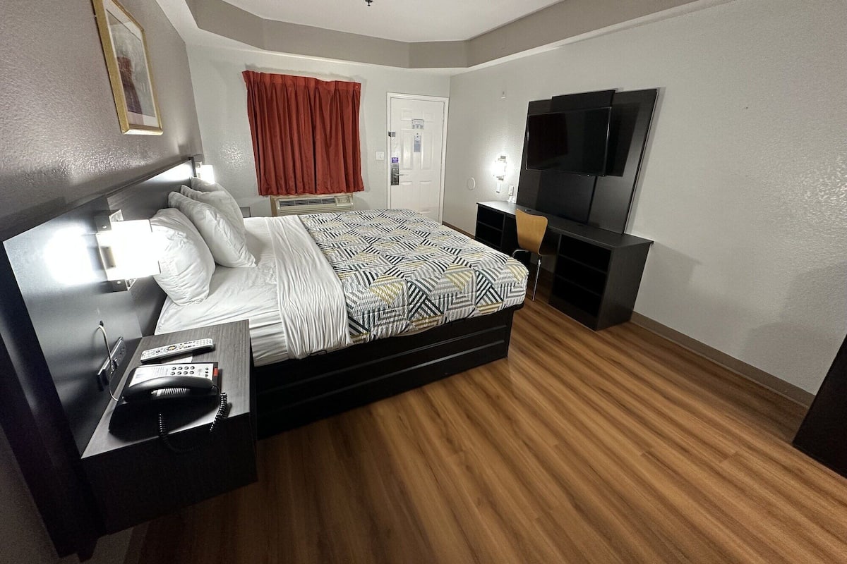 Une chambre d’hôtel moderne avec un lit, une table de chevet avec un téléphone, une télévision et un rideau rouge.