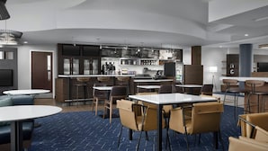 Un hall d’hôtel moderne doté d’un bar, de différents espaces de détente et d’un grand écran.