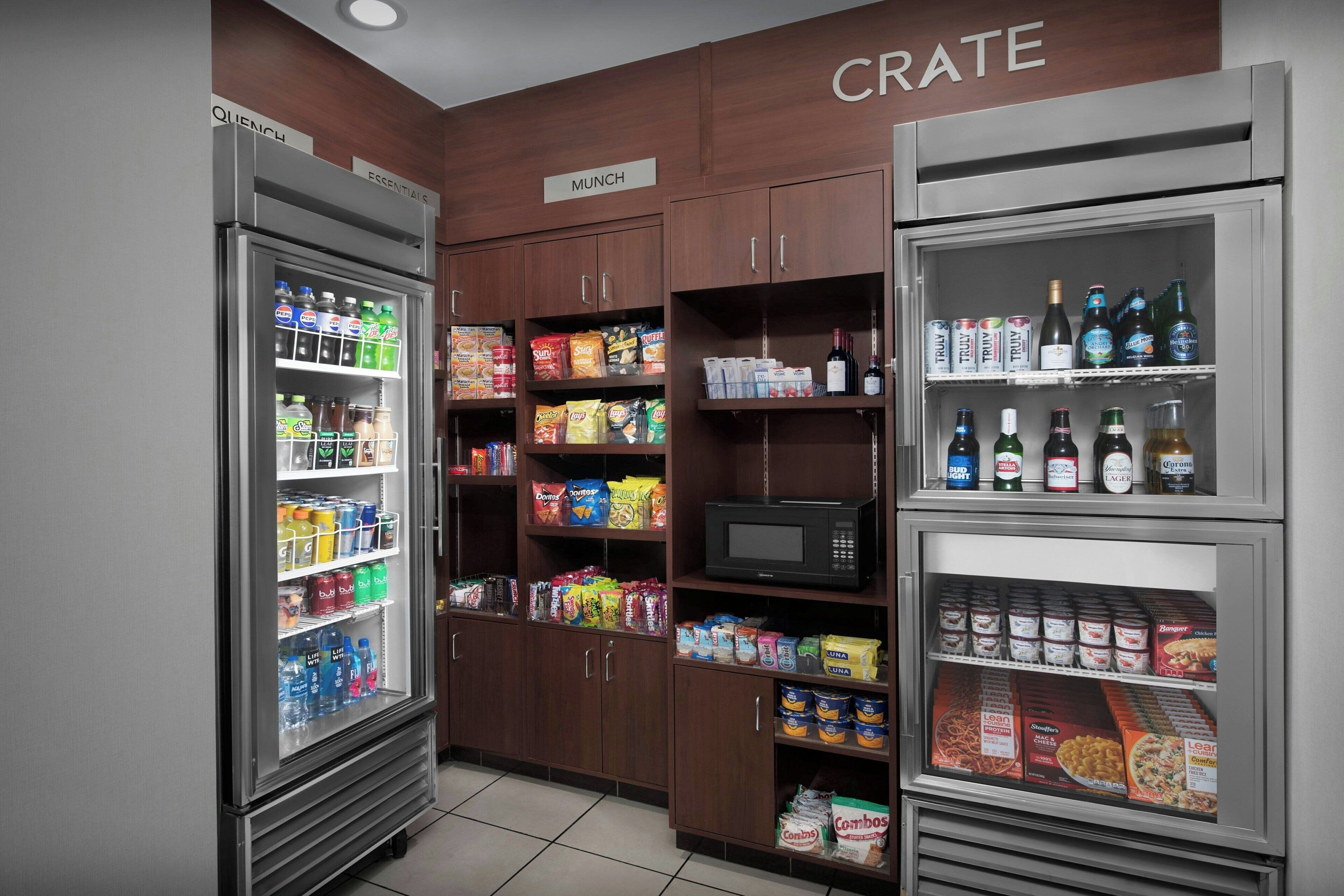 A kitchenette with a refrigerator, microwave, and pantry stocked with snacks, beverages, and condiments.