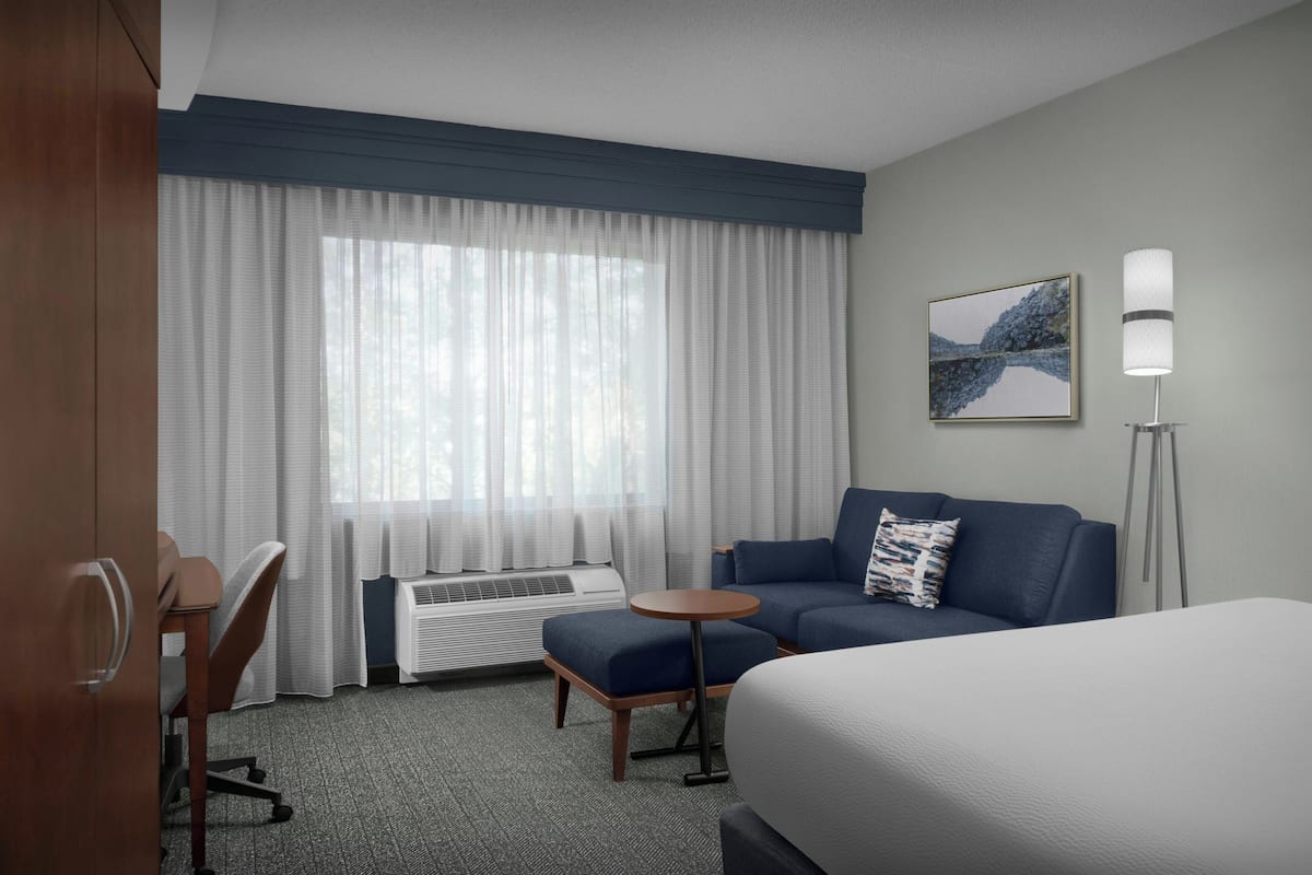 A hotel room with a bed, a sofa, a small table, a desk, and a window with curtains.