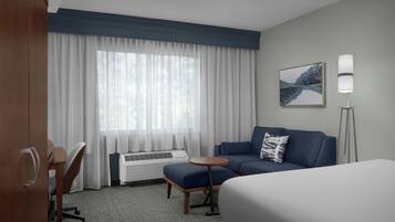 A hotel room with a bed, a sofa, a small table, a desk, and a window with curtains.
