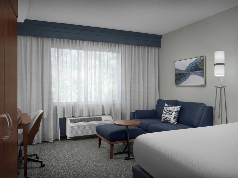 A hotel room with a bed, a sofa, a small table, a desk, and a window with curtains.