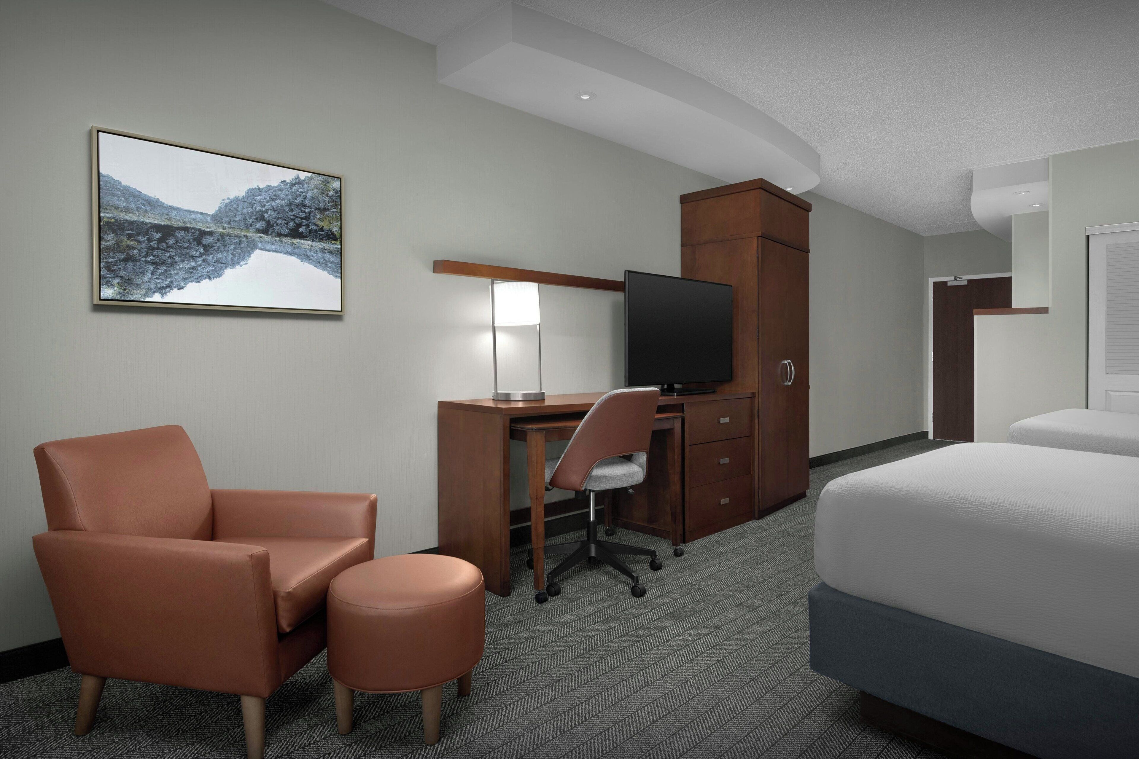 Una habitación de hotel con cama, escritorio con silla, televisor, armario y un cuadro en la pared.