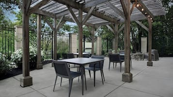 Eine Terrasse im Freien mit Tischen und Stühlen, einer Holz-Pergola und einem Zaun.