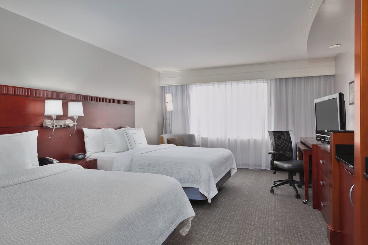 Une chambre d’hôtel avec deux lits, un bureau avec un ordinateur, une chaise et un téléviseur.