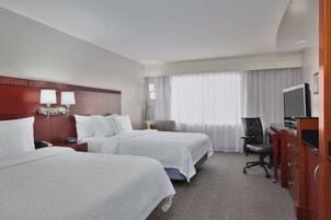 A hotel room with two beds, a desk with a computer, a chair, and a TV.