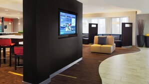 A modern hotel lobby with a large screen displaying a map, a seating area with a sofa and chairs, and a reception desk. - Courtyard by Marriott Corpus Christi (Corpus Christi)