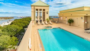 A swimming pool with a view of the water, a gazebo, and a building with a green roof.