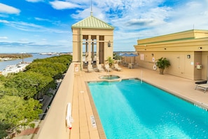 A swimming pool with a view of the water, a gazebo, and a building with a green roof.
