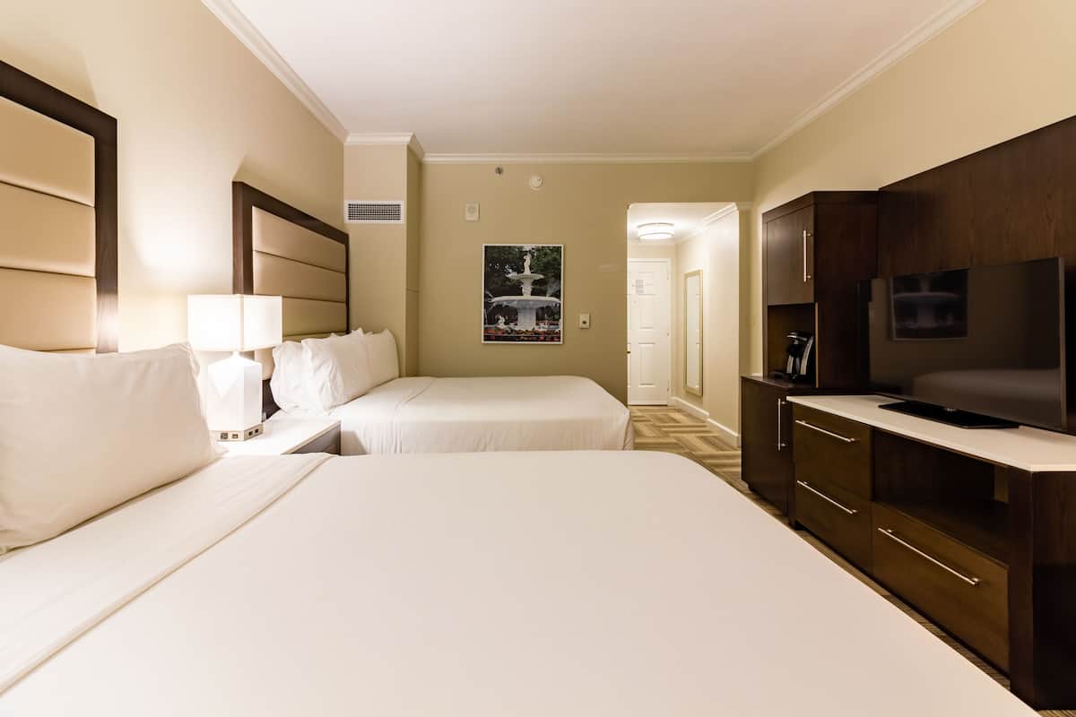 A hotel room with two beds, a TV, a minibar, and a painting on the wall.