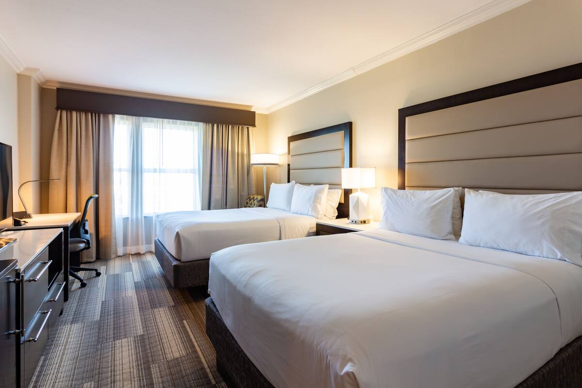 A hotel room with two beds, a desk, a chair, and a TV.