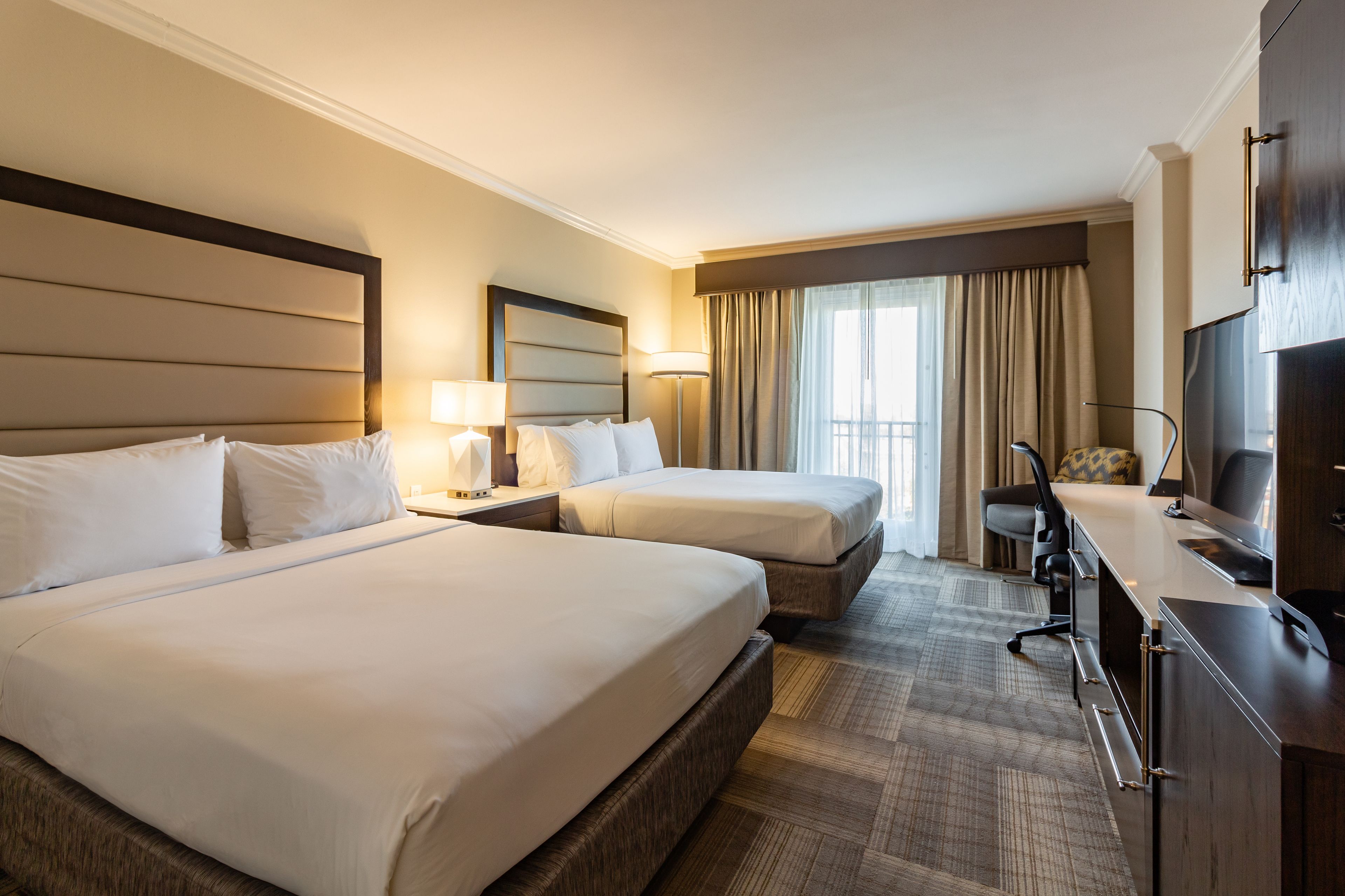 A hotel room with two beds, a desk, a chair, and a TV.