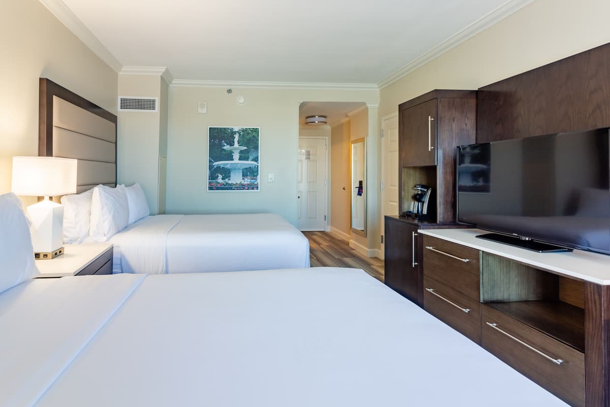 A hotel room with two beds, a TV, a coffee maker, and a painting on the wall.