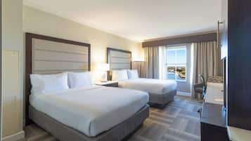 Une chambre d’hôtel avec deux lits, un bureau, une chaise et une grande fenêtre avec des rideaux.
