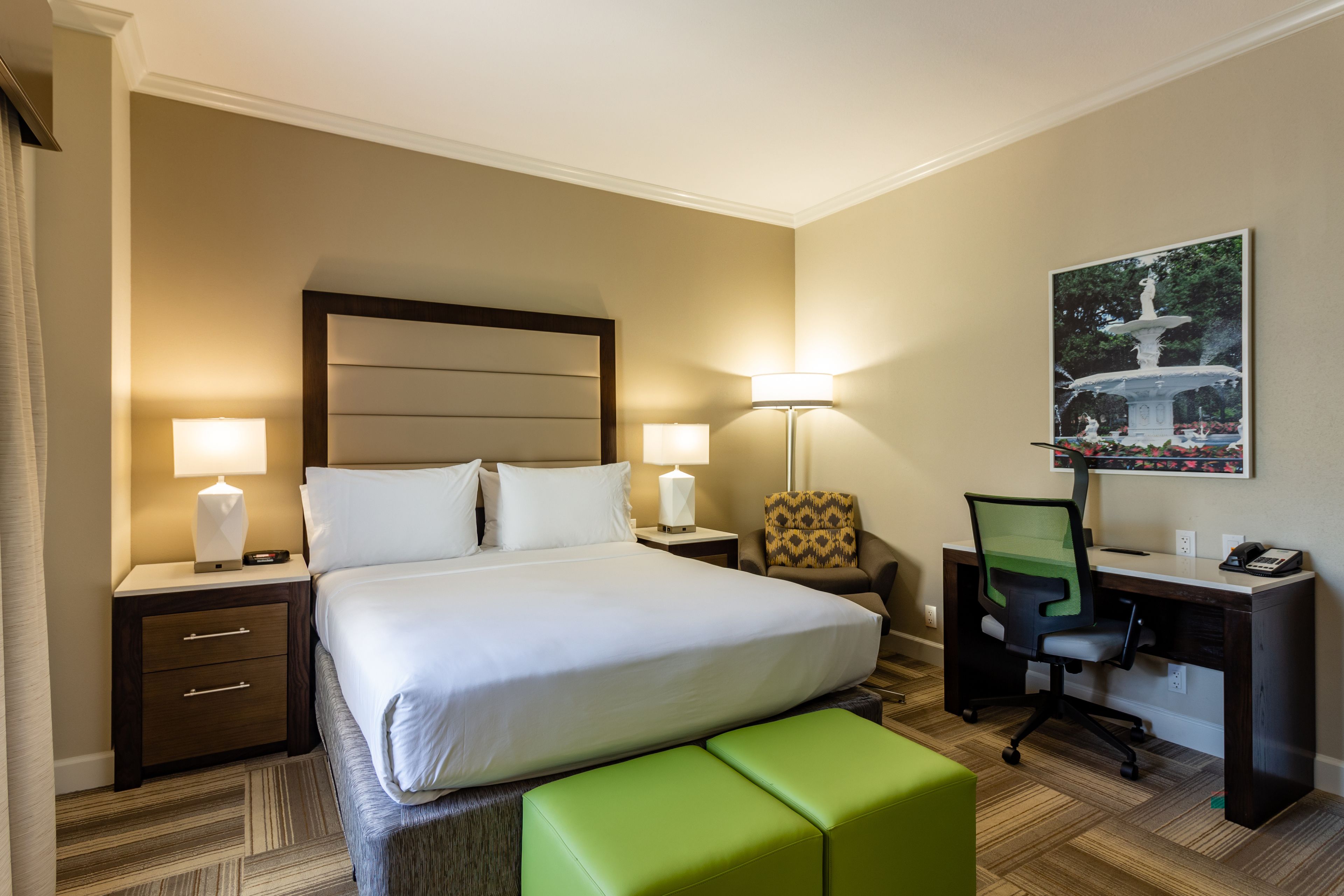 Habitación de hotel con una cama grande, dos mesitas de noche con lámparas, un escritorio con una silla y un cuadro en la pared.