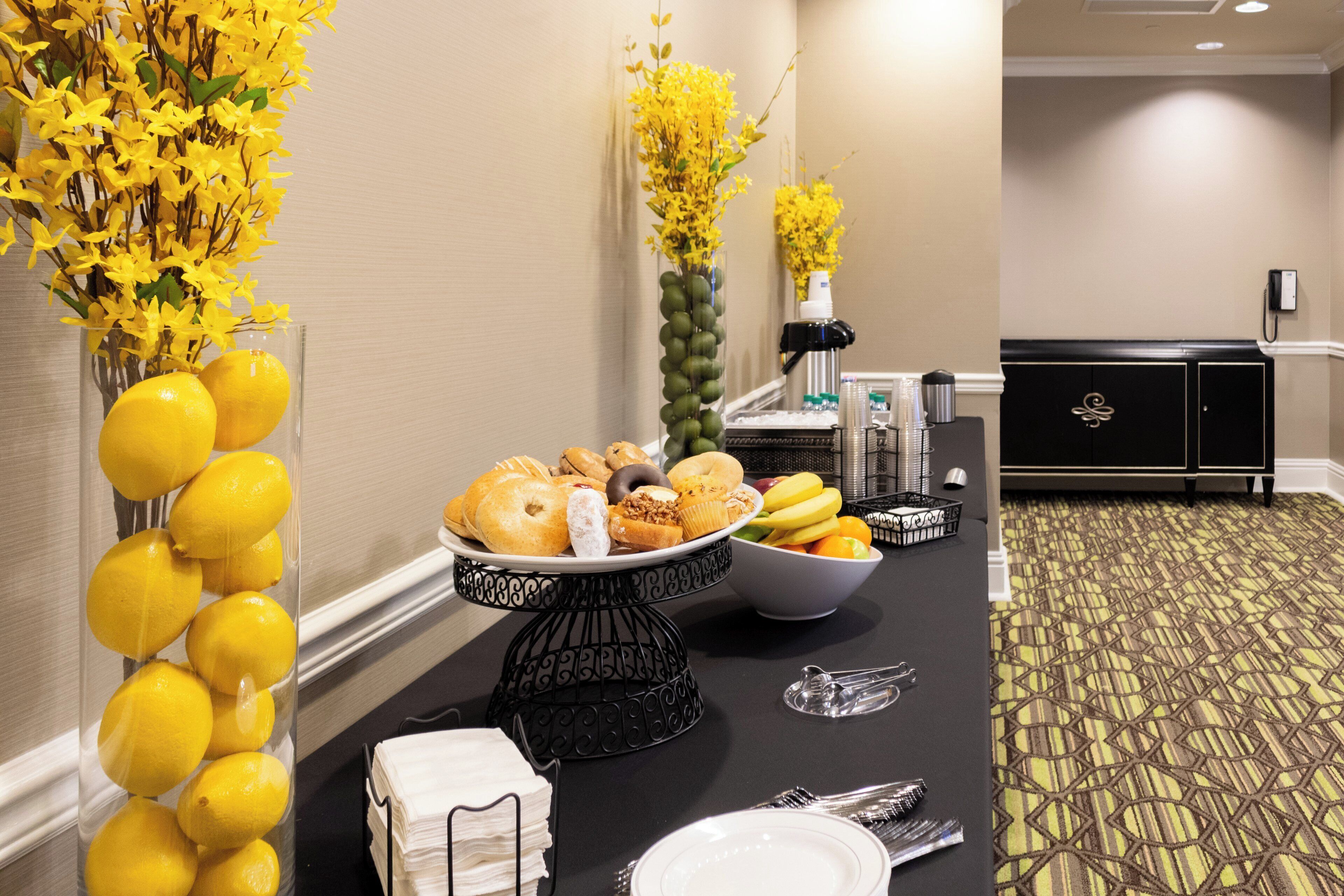 A buffet setup with a variety of food items, a vase with yellow flowers, and a coffee machine.