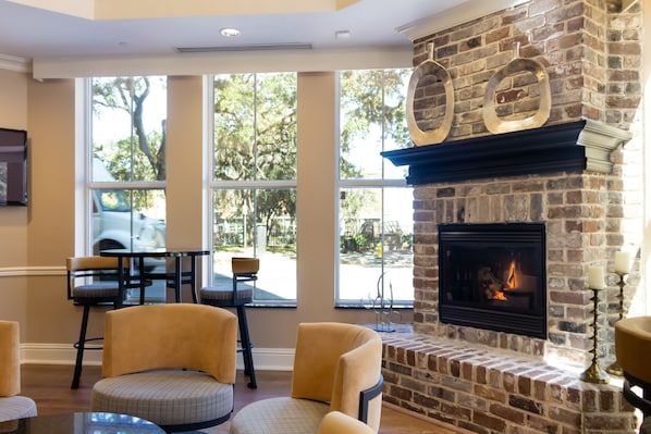 A cozy room with a brick fireplace, comfortable seating, and large windows offering a view of the outdoors. - Holiday Inn Express Savannah - Historic District by IHG (Savannah)