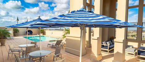A rooftop pool area with lounge chairs, a pool, and a striped umbrella.