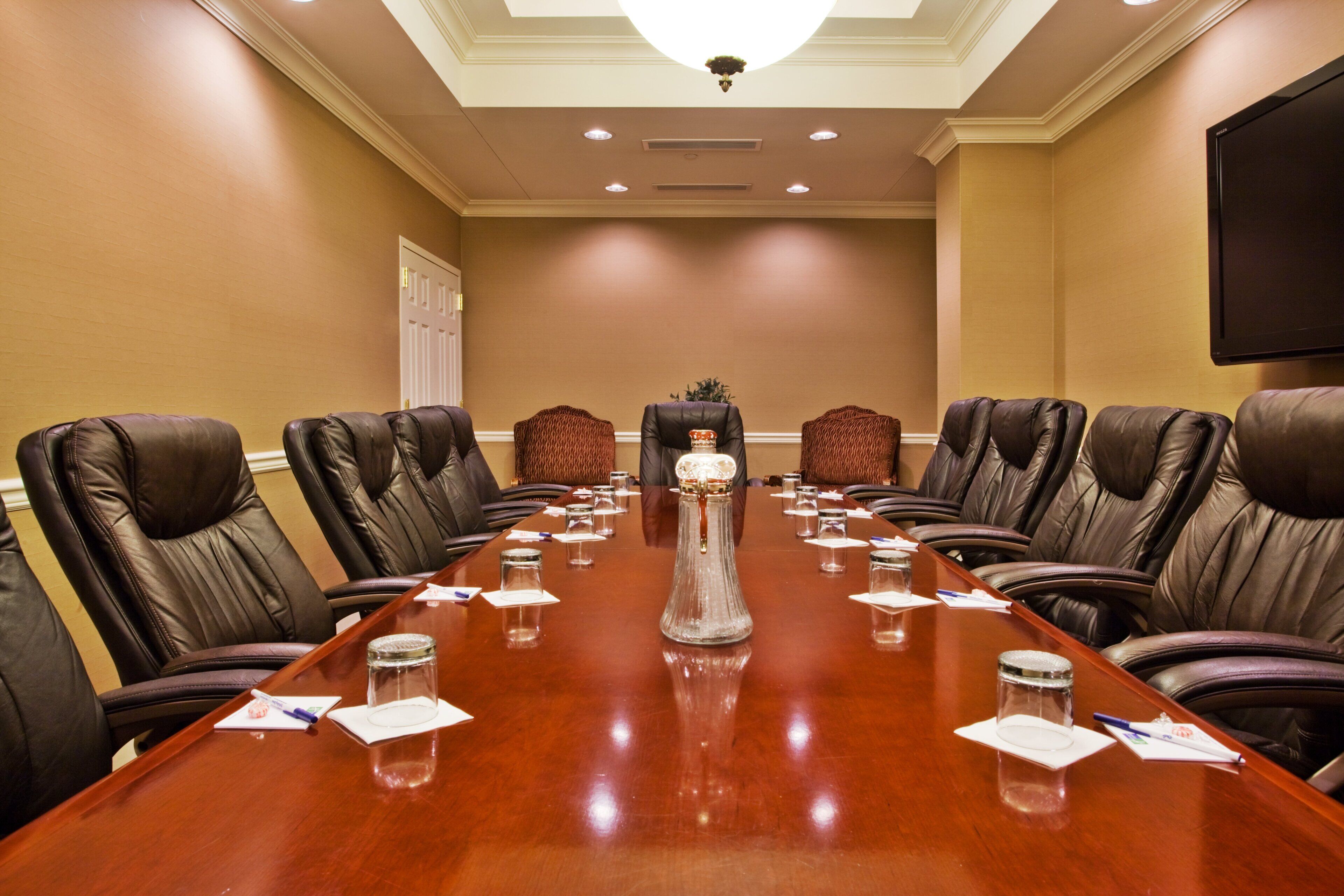 A conference room with a long table, leather chairs, and a large screen.
