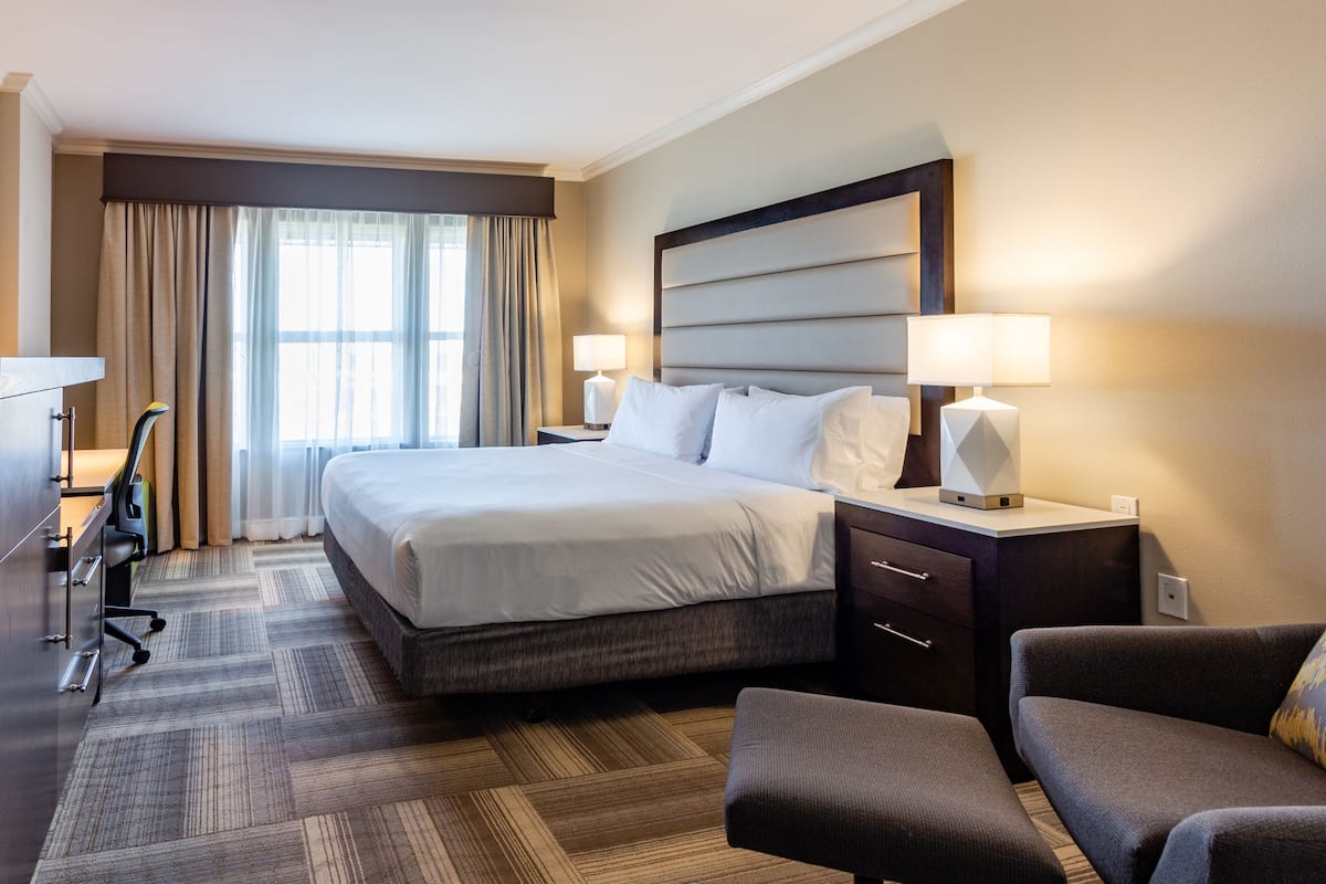 A hotel room with a large bed, two bedside tables with lamps, a desk with a chair, and a sofa.