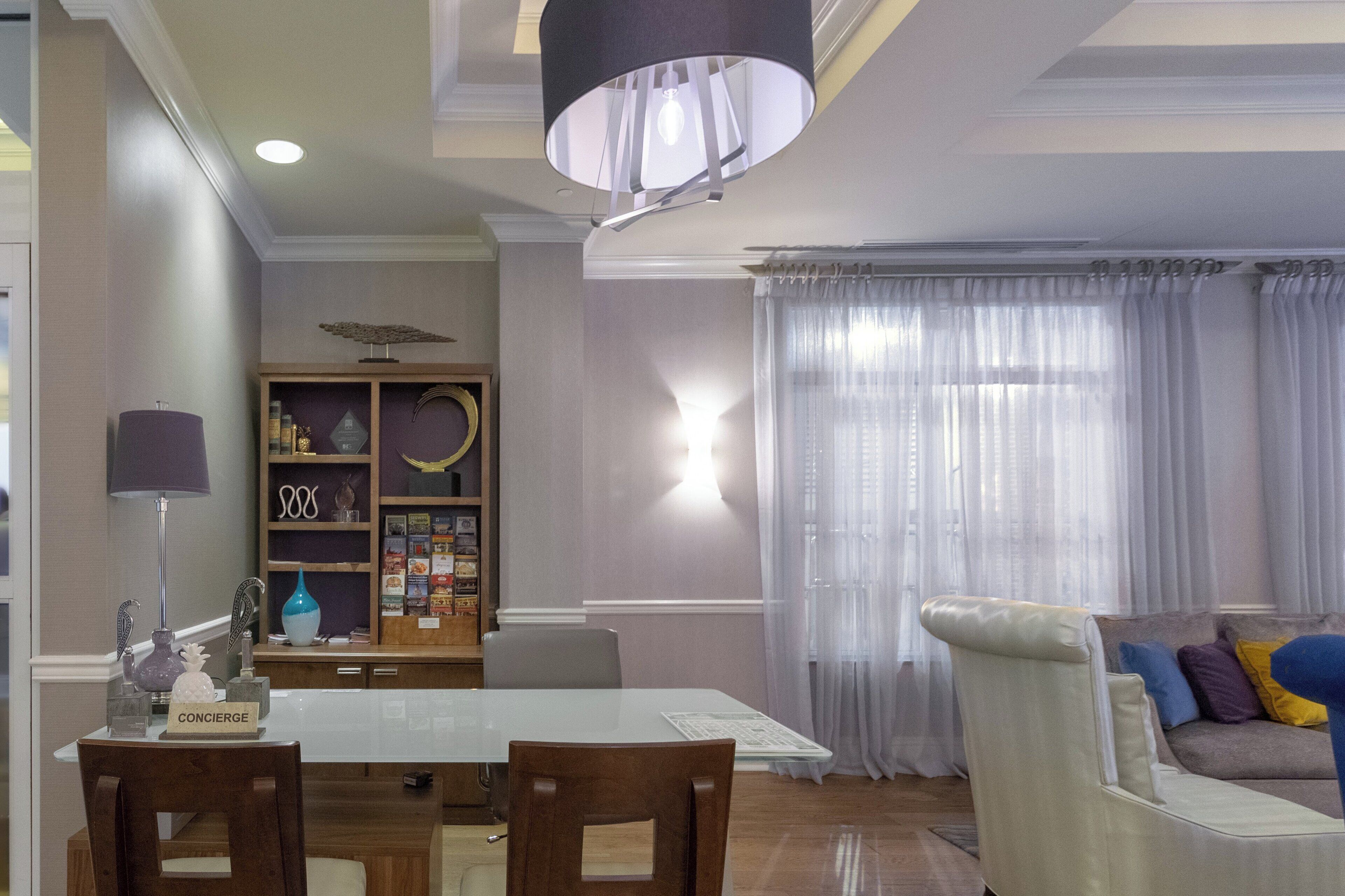 Un área de comedor con una mesa, sillas, una estantería y un sofá con cojines.