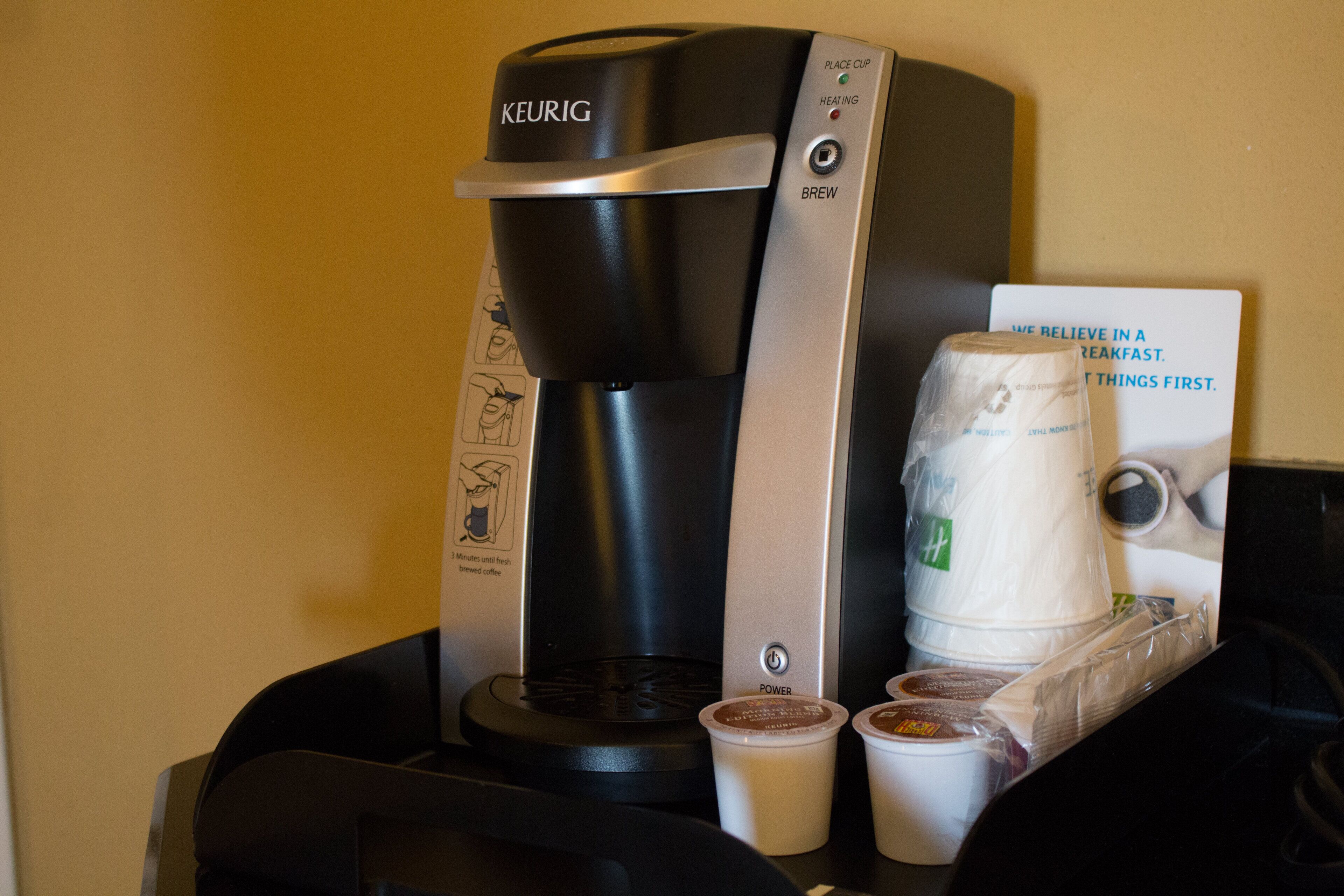 A Keurig coffee maker with a cup of coffee and a reusable cup on a table.