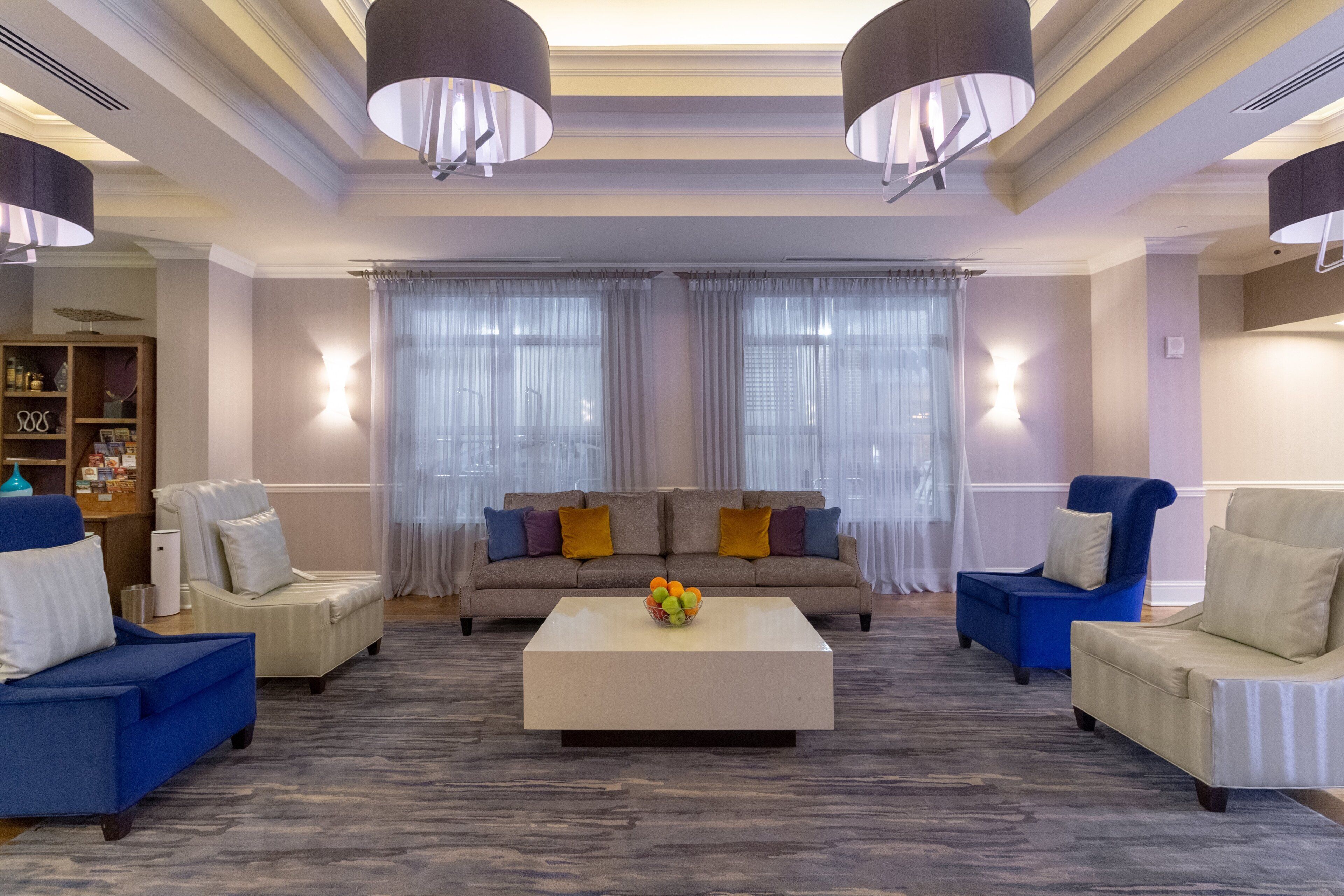 A spacious living room with a neutral color palette, featuring a sofa set, armchairs, a coffee table, and a bookshelf.