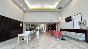 A modern hotel lobby with a reception desk, seating area, and a large wall with a map and artwork.