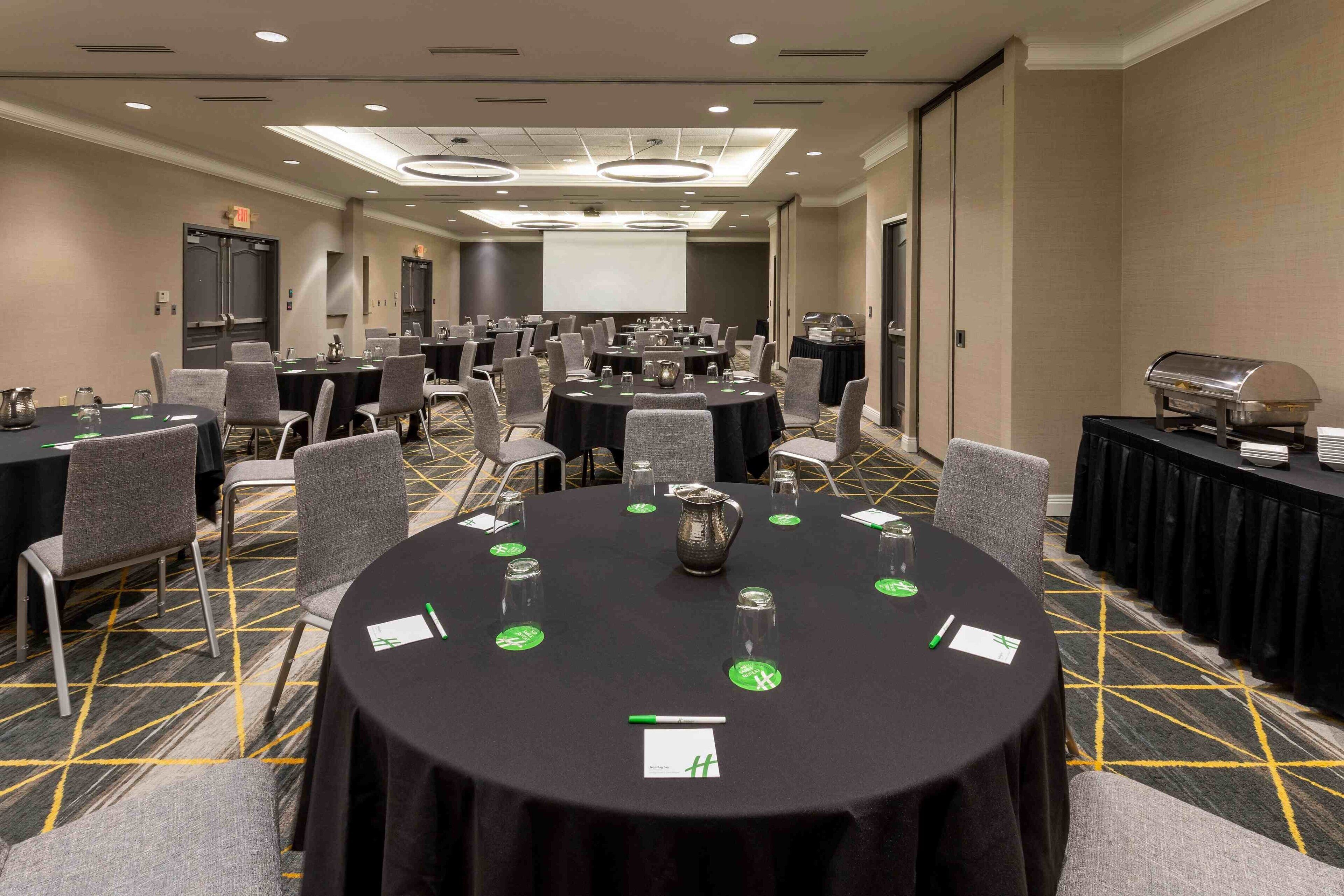 A conference room with multiple tables, chairs, and a projector screen.