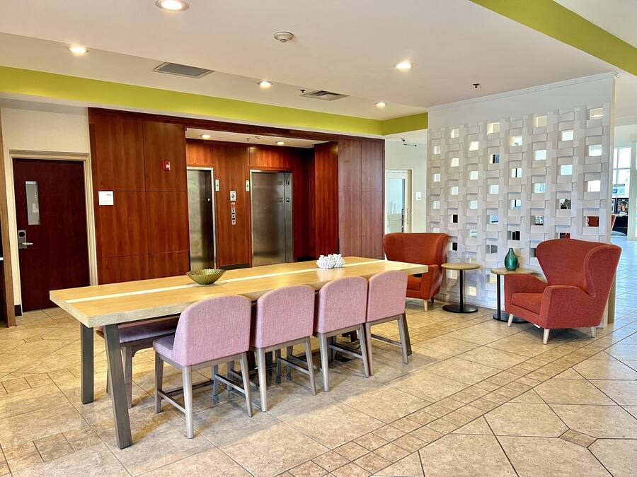 Un comedor moderno con una mesa larga, sillas rosas y un sillón rojo.