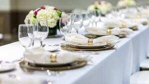 A long table set with white tablecloths, gold-rimmed plates, and clear wine glasses.