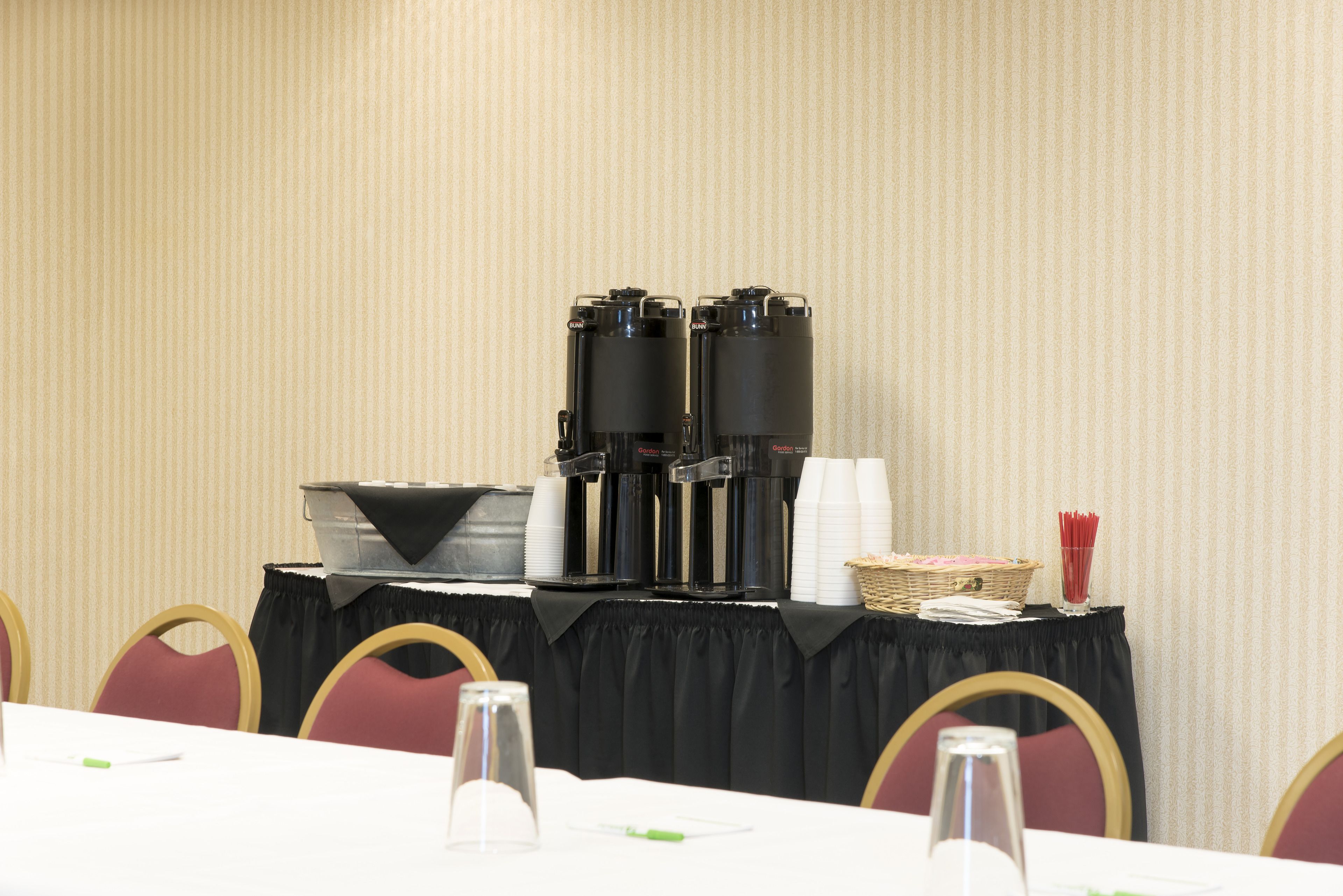 A conference room with a table set for a meeting, equipped with coffee machines, cups, and a basket of napkins.