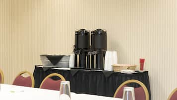 A conference room with a table set for a meeting, equipped with coffee machines, cups, and a basket of napkins.