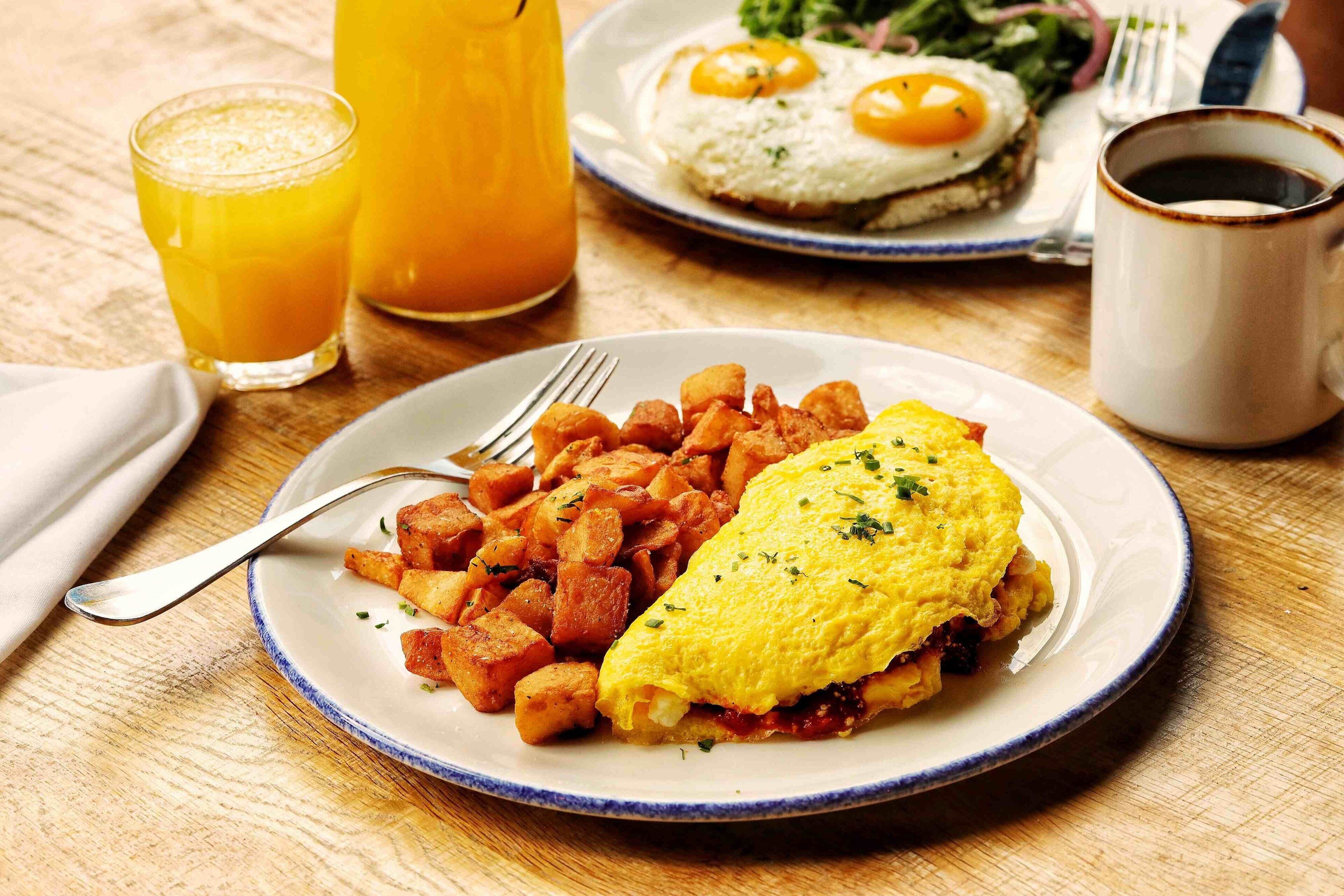 Ein Frühstücksteller mit Omelett und Rösti, ein Glas Orangensaft und eine Kaffeetasse auf einem Holztisch.