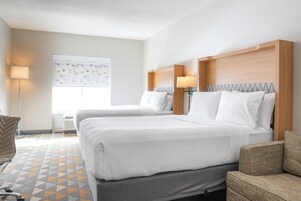 Habitación de hotel con dos camas, un escritorio, una silla y un ventanal amplio.