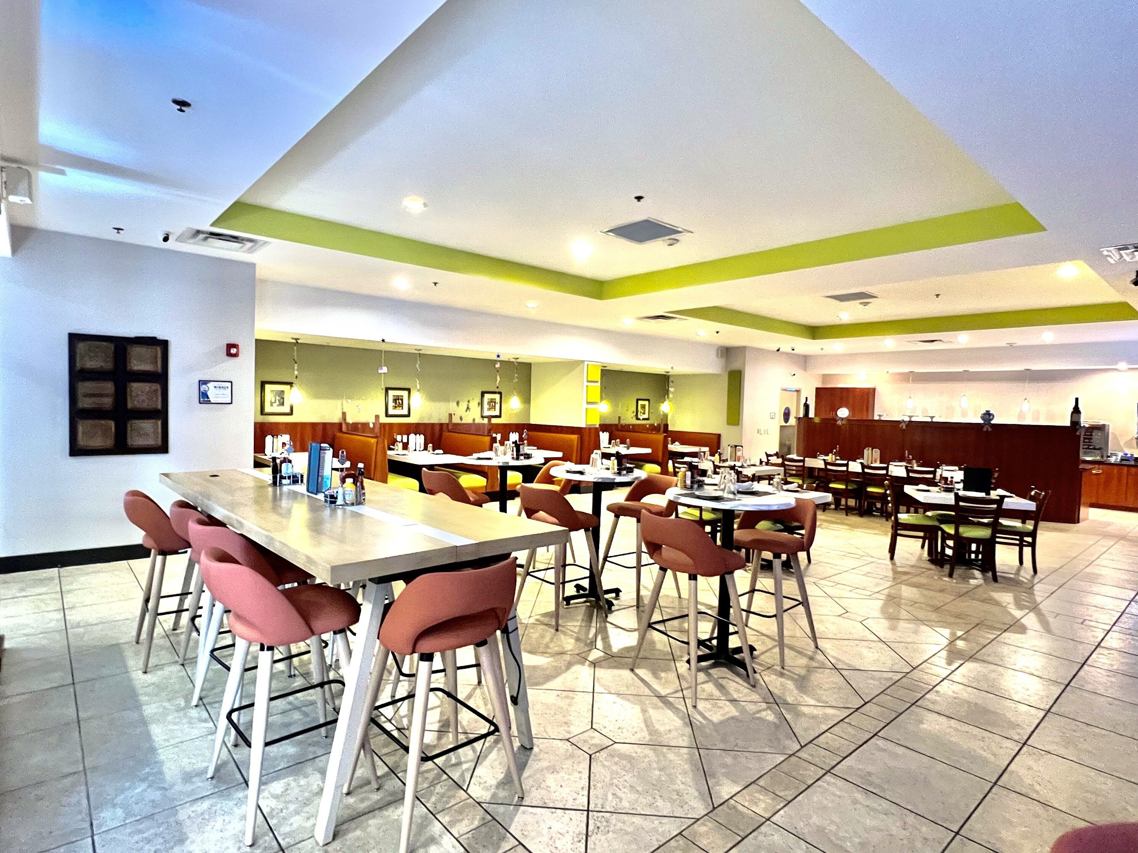 Un restaurante espacioso con varias mesas y cabinas, una zona de cocina y un interior limpio y moderno.