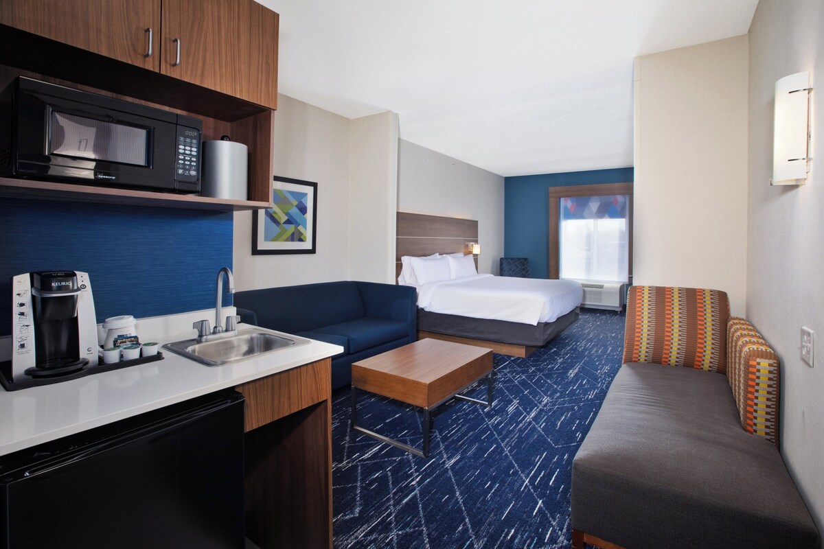 Habitació d'hotel amb cuina americana, un llit, un sofà i una taula petita.