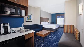 A hotel room with a kitchenette, a bed, a sofa, and a small table.