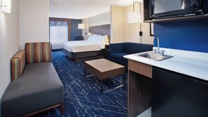 A hotel room with a bed, a sofa, a small table, a microwave, and a sink.