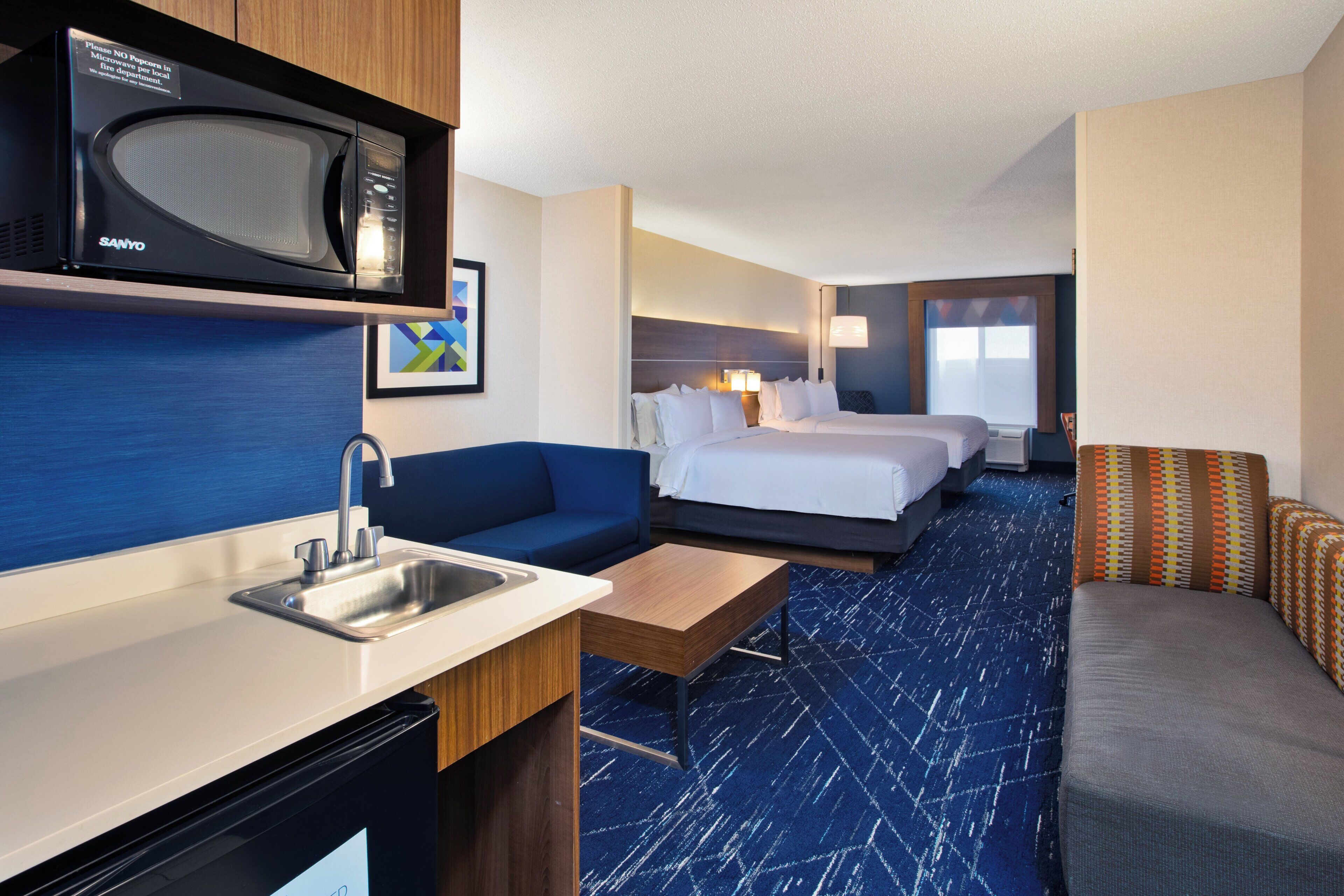 A hotel room with a kitchenette, a bed, a sofa, and a desk.