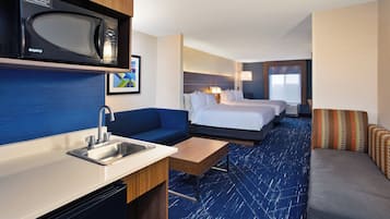 A hotel room with a kitchenette, a bed, a sofa, and a desk.