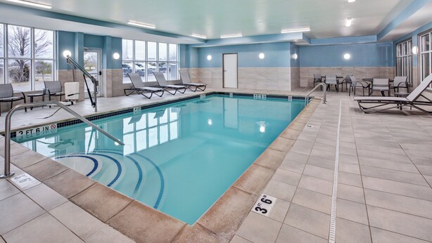 A pool area with lounge chairs, a pool ladder, and a clear view of the outside through large windows. - Holiday Inn Express Hotel & Suites Auburn Hills by IHG (Auburn Hills)