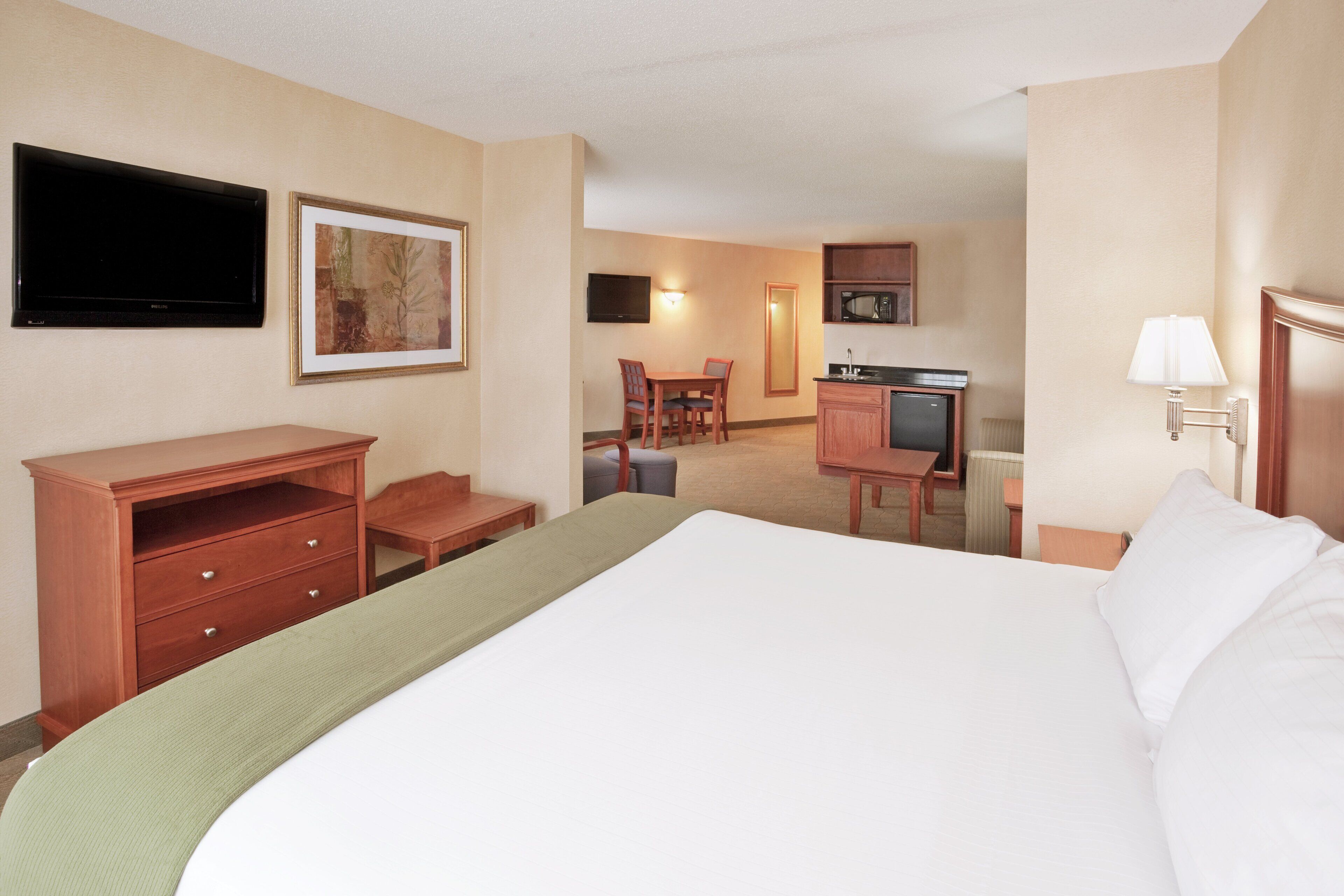 Una habitación de hotel con cama, escritorio, silla, televisor y microondas.