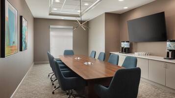 A conference room with a long table, blue chairs, a mounted TV, and artwork on the walls.