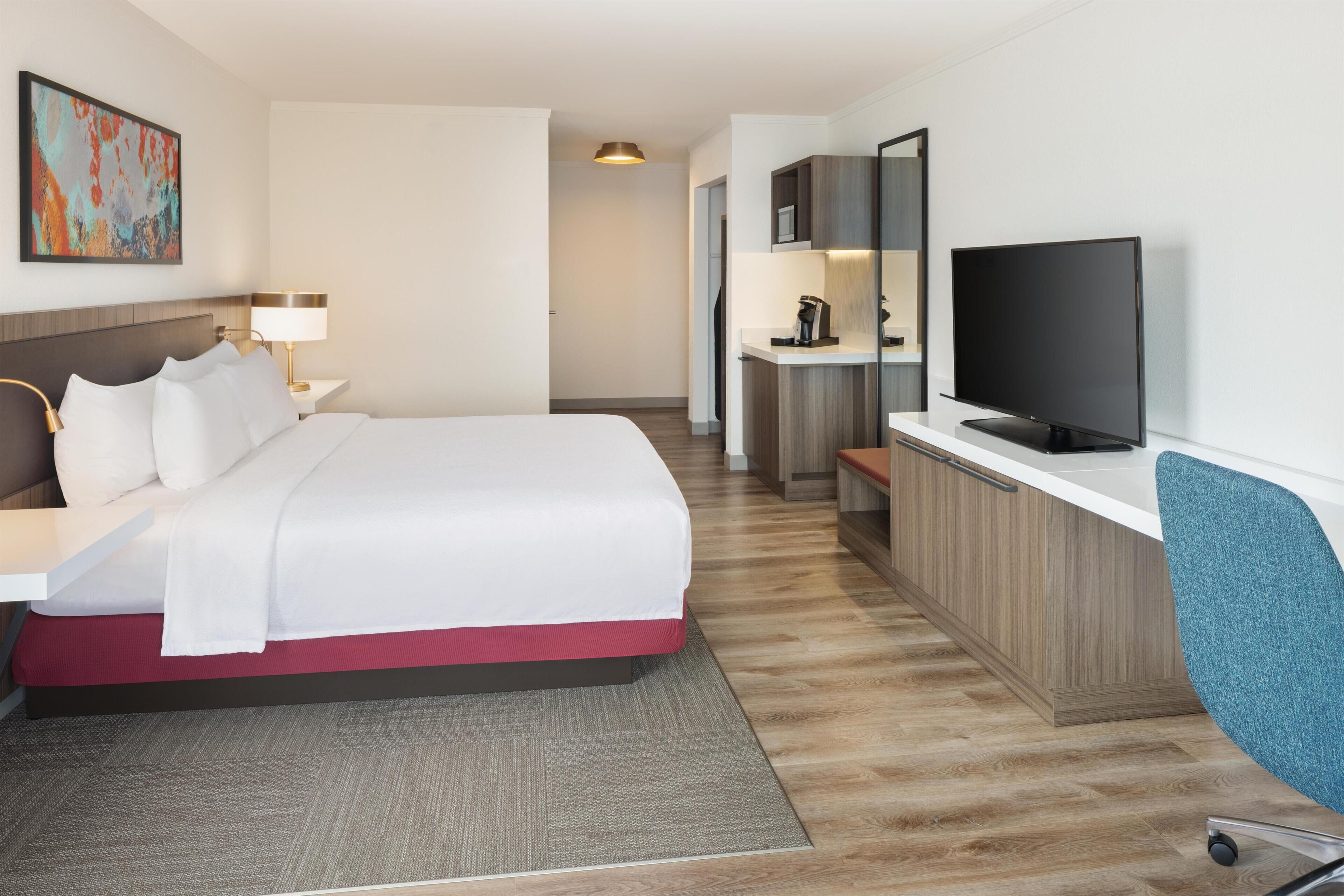 A hotel room with a bed, a desk, a television, and a kitchenette.