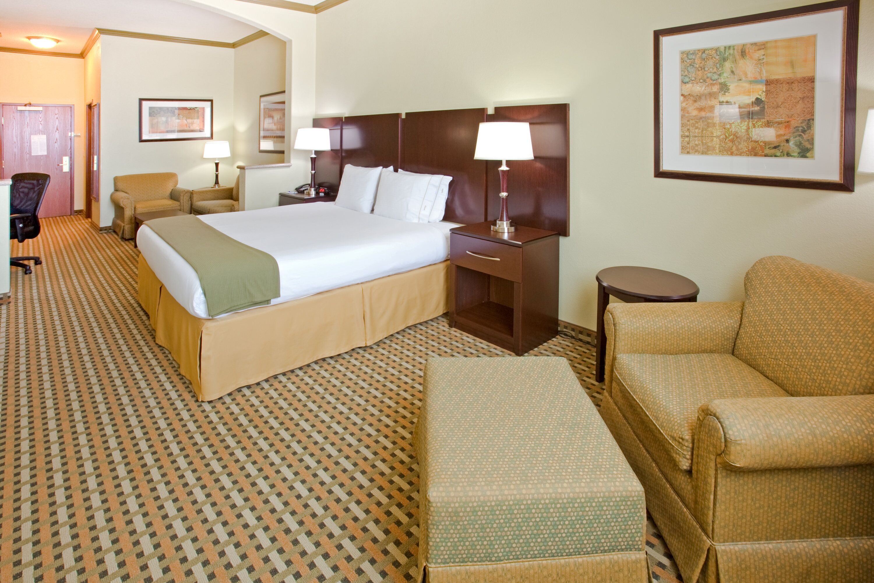 A hotel room with a large bed, two bedside tables with lamps, a chair, a sofa, and a patterned carpet.