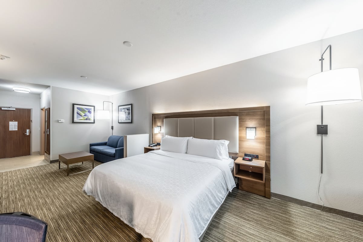 A hotel room with a large bed, a desk, a chair, a lamp, and a wall-mounted TV.