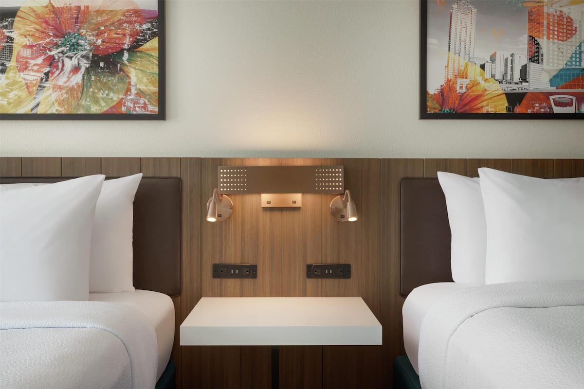 Habitación de hotel con dos camas, una mesa en el centro y obras de arte en las paredes.
